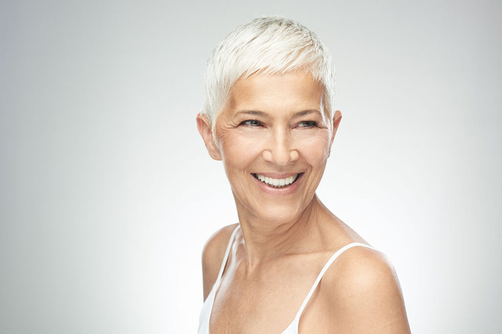 Beautiful smiling senior woman with short gray hair posing in front of gray background. Beauty photography.