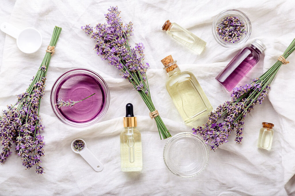 Lavender oils serum and lavender flowers on white fabric. Skincare cosmetics products. Set natural spa beauty products. Lavender essential oil, serum, body butter, massage oil, liquid. Flat lay.